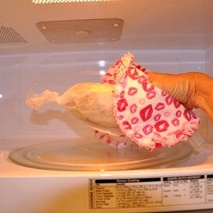 May include: A white microwave with a glass turntable. A pink and white fabric with a lip print is being placed inside the microwave.
