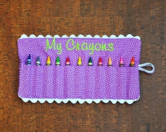 May include: Purple fabric crayon holder with white polka dots and a scalloped edge. The holder has 10 slots for crayons and says "My Crayons" in green embroidery.