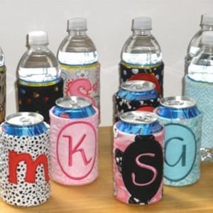 May include: Nine personalized beverage insulators with various patterns and colors. Each insulator has a different letter embroidered on it. The insulators are surrounding water bottles.