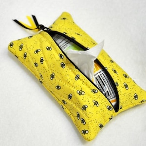 May include: Yellow quilted tissue box cover with a zipper closure and a black and white bee pattern. The cover is open and a tissue box is partially visible inside.