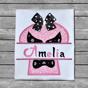 May include: Pink and black embroidered design of a skull with a bow on top and the name Amelia written below.