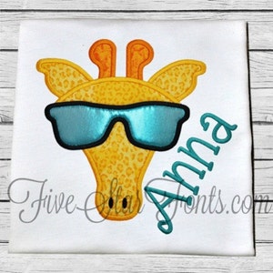 May include: A yellow and orange giraffe wearing blue sunglasses with the name "Anna" embroidered in teal on a white background.