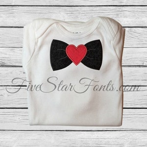 Può includere: Un body bianco per neonato con un papillon nero con un cuore rosso al centro.