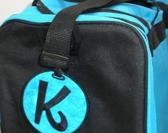 May include: A blue and black duffel bag with a large, circular, turquoise logo featuring a stylized black letter "K".