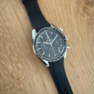 May include: A black wristwatch with a black rubber strap. The watch face is dark gray with silver accents and multiple sub-dials. The bezel has a tachymeter scale. The watch is labeled "SWISS MADE".