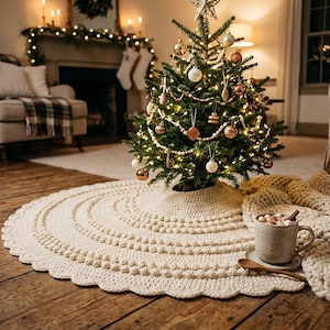 May include: A round, cream-colored crocheted Christmas tree skirt featuring a textured bobble stitch pattern and a scalloped edge. The skirt is placed on a wooden floor beneath a decorated evergreen tree with warm lights and gold ornaments.