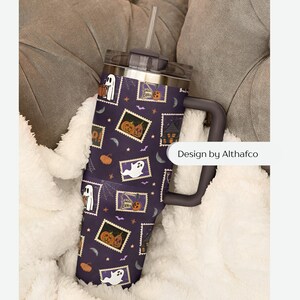 May include: A dark purple stainless steel tumbler with a handle, a clear lid, and a straw. The exterior features a repeating pattern of postage stamp-style illustrations depicting ghosts, pumpkins, and haunted houses. The text Design by Althafco is visible.