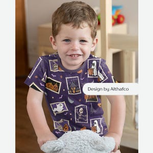 May include: A short-sleeved purple t-shirt featuring a repeating pattern of rectangular postage stamp graphics. The prints include illustrations of ghosts, pumpkins, skeletons, and a haunted house. The text Design by Althafco is visible.