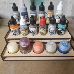 May include: A wooden display stand with multiple bottles of acrylic paints and inks. The bottles are in various colours, including black, white, orange, and silver. Some bottles have labels with text like "MODEL AIR" and "WARPAIN".