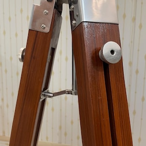Vintage-style adjustable tripod stand handcrafted from premium teak wood with polished aluminium and nickel hardware. Features three sturdy wooden legs, an adjustable center column, and a height range of 25 to 50 inches. Ideal for DIY photo booths, DSLR cameras, floor lamps, studio décor, and nautical-inspired interiors. Handcrafted wooden tripod with a timeless industrial design.