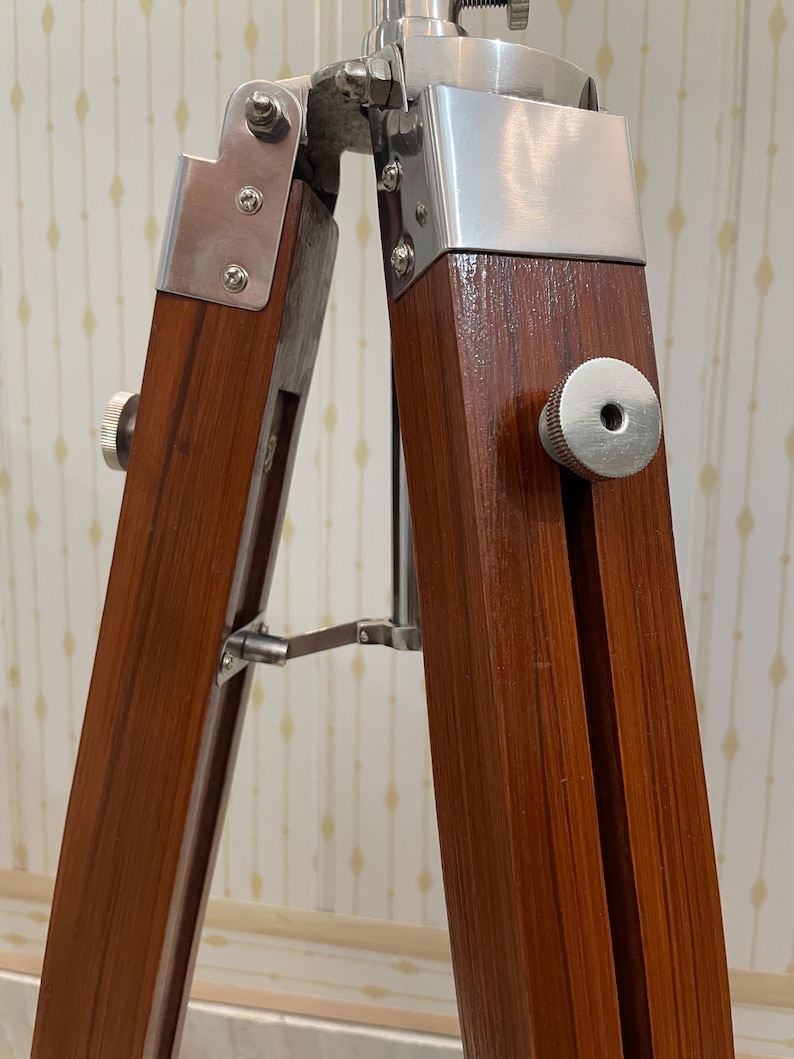 Vintage-style adjustable tripod stand handcrafted from premium teak wood with polished aluminium and nickel hardware. Features three sturdy wooden legs, an adjustable center column, and a height range of 25 to 50 inches. Ideal for DIY photo booths, DSLR cameras, floor lamps, studio décor, and nautical-inspired interiors. Handcrafted wooden tripod with a timeless industrial design.