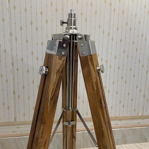 Vintage-style adjustable tripod stand handcrafted from premium teak wood with polished aluminium and nickel hardware. Features three sturdy wooden legs, an adjustable center column, and a height range of 25 to 50 inches. Ideal for DIY photo booths, DSLR cameras, floor lamps, studio décor, and nautical-inspired interiors. Handcrafted wooden tripod with a timeless industrial design.