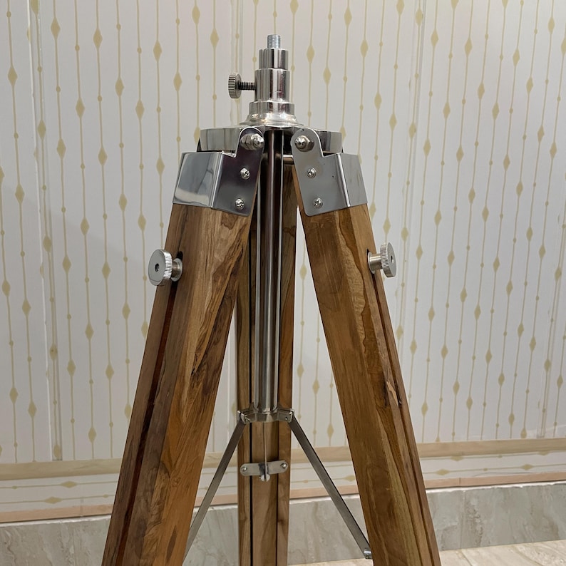 Vintage-style adjustable tripod stand handcrafted from premium teak wood with polished aluminium and nickel hardware. Features three sturdy wooden legs, an adjustable center column, and a height range of 25 to 50 inches. Ideal for DIY photo booths, DSLR cameras, floor lamps, studio décor, and nautical-inspired interiors. Handcrafted wooden tripod with a timeless industrial design.