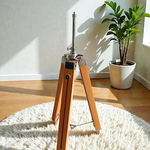 Vintage-style adjustable tripod stand handcrafted from premium teak wood with polished aluminium and nickel hardware. Features three sturdy wooden legs, an adjustable center column, and a height range of 25 to 50 inches. Ideal for DIY photo booths, DSLR cameras, floor lamps, studio décor, and nautical-inspired interiors. Handcrafted wooden tripod with a timeless industrial design.