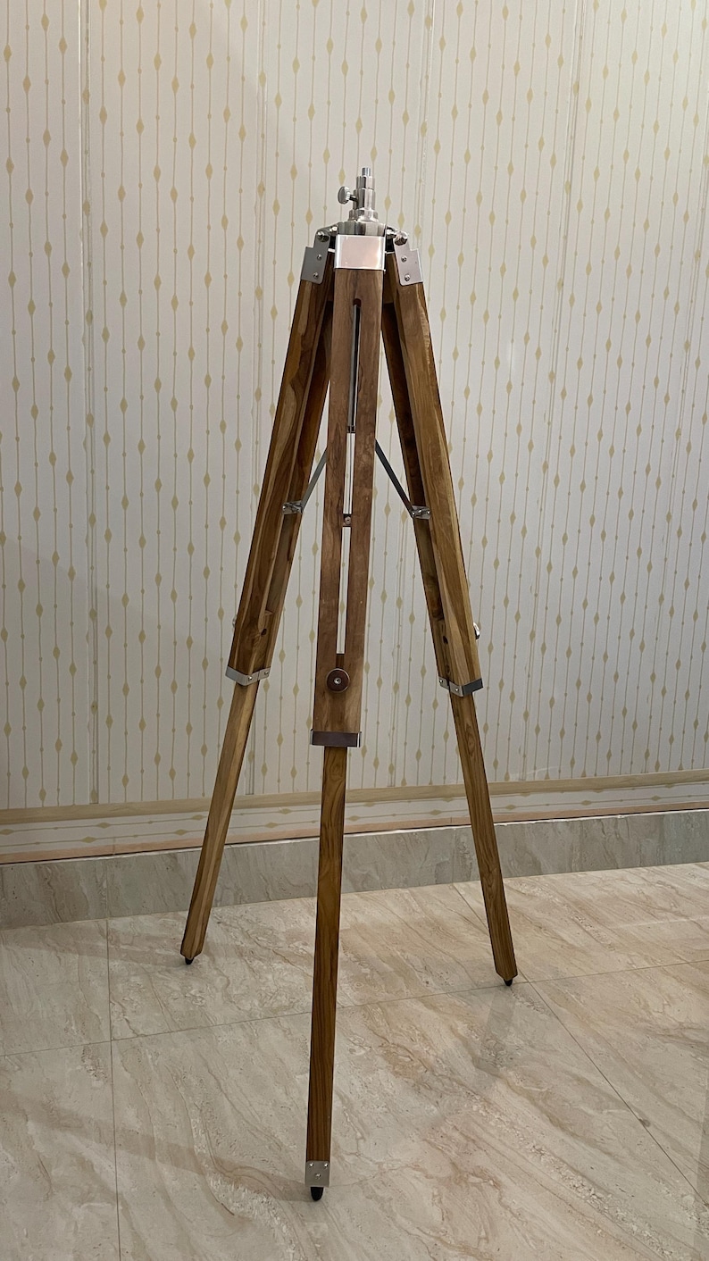 A natural wood tripod easel stand with splayed legs for stability For a plant/decorative stand: "Rustic wooden tripod plant stand with angled legs joined at the top.Vintage-style adjustable tripod stand handcrafted from premium teak wood with polished aluminium and nickel hardware. Features three sturdy wooden legs, an adjustable center column, and a height range of 25 to 50 inches. Ideal for DIY photo booths, DSLR cameras, floor lamps, studio décor, and nautical-inspired interiors.