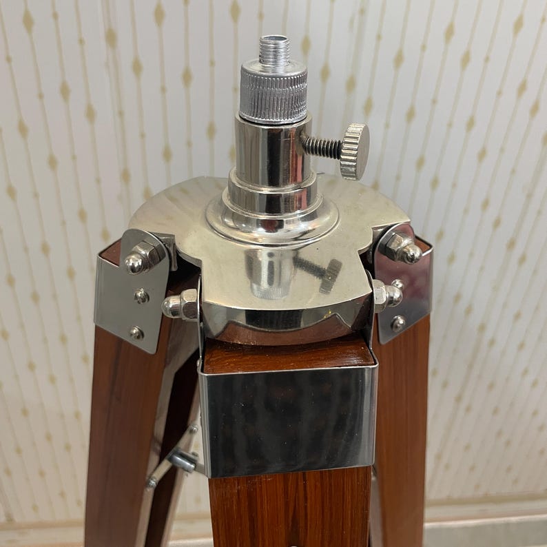Vintage-style adjustable tripod stand handcrafted from premium teak wood with polished aluminium and nickel hardware. Features three sturdy wooden legs, an adjustable center column, and a height range of 25 to 50 inches. Ideal for DIY photo booths, DSLR cameras, floor lamps, studio décor, and nautical-inspired interiors. Handcrafted wooden tripod with a timeless industrial design.