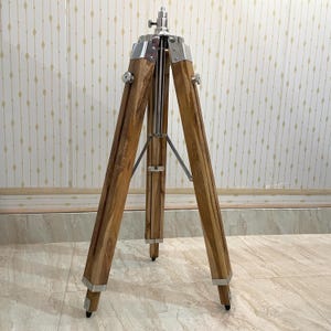 Vintage-style adjustable tripod stand handcrafted from premium teak wood with polished aluminium and nickel hardware. Features three sturdy wooden legs, an adjustable center column, and a height range of 25 to 50 inches. Ideal for DIY photo booths, DSLR cameras, floor lamps, studio décor, and nautical-inspired interiors. Handcrafted wooden tripod with a timeless industrial design.