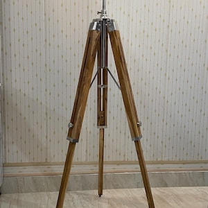 Vintage-style adjustable tripod stand handcrafted from premium teak wood with polished aluminium and nickel hardware. Features three sturdy wooden legs, an adjustable center column, and a height range of 25 to 50 inches. Ideal for DIY photo booths, DSLR cameras, floor lamps, studio décor, and nautical-inspired interiors. Handcrafted wooden tripod with a timeless industrial design.