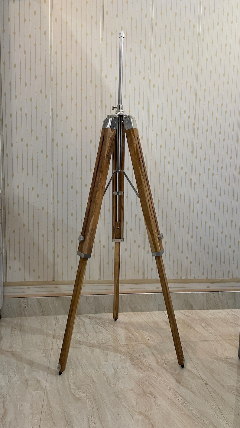 Vintage-style adjustable tripod stand handcrafted from premium teak wood with polished aluminium and nickel hardware. Features three sturdy wooden legs, an adjustable center column, and a height range of 25 to 50 inches. Ideal for DIY photo booths, DSLR cameras, floor lamps, studio décor, and nautical-inspired interiors. Handcrafted wooden tripod with a timeless industrial design.