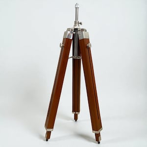 Vintage-style adjustable tripod stand handcrafted from premium teak wood with polished aluminium and nickel hardware. Features three sturdy wooden legs, an adjustable center column, and a height range of 25 to 50 inches. Ideal for DIY photo booths, DSLR cameras, floor lamps, studio décor, and nautical-inspired interiors. Handcrafted wooden tripod with a timeless industrial design.