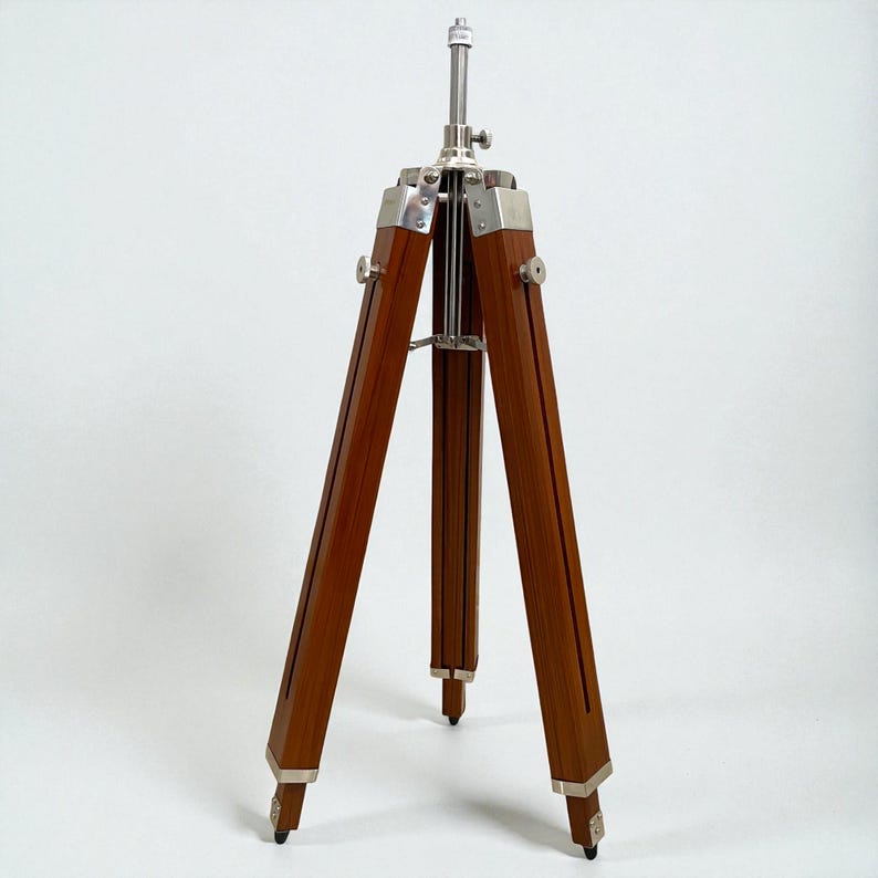 Vintage-style adjustable tripod stand handcrafted from premium teak wood with polished aluminium and nickel hardware. Features three sturdy wooden legs, an adjustable center column, and a height range of 25 to 50 inches. Ideal for DIY photo booths, DSLR cameras, floor lamps, studio décor, and nautical-inspired interiors. Handcrafted wooden tripod with a timeless industrial design.
