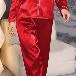 Puede incluir: Un conjunto de pijama de satén rojo con mangas largas y pantalones. El conjunto tiene ribetes blancos alrededor del cuello, los puños y los bolsillos.
