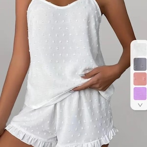 May include: White two-piece pajama set with a sleeveless top and shorts. The top and shorts have a white polka dot pattern and a ruffled trim.