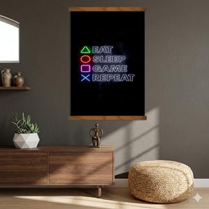 Op de afbeelding: Een zwarte wanddecoratie met de woorden "EAT SLEEP GAME REPEAT" in witte neonletters. De tekst wordt vergezeld door groene, rode, paarse en blauwe geometrische vormen. Het kunstwerk is omlijst met houten staven.