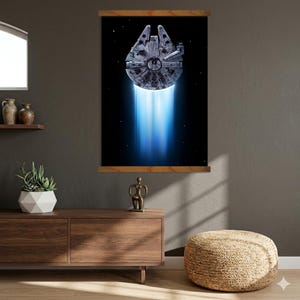 Könnte beinhalten: Ein gerahmter Wandkunstdruck mit dem Raumschiff Millennium Falcon vor einem schwarzen Weltraumhintergrund. Das Raumschiff ist in Grautönen detailliert, mit hellem blauem Licht, das von unten ausgeht. Der Druck ist auf Holzleisten montiert.