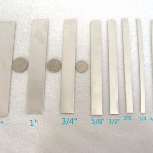May include: A set of ten metal strips in various widths, ranging from 1/8 inch to 1.5 inches. The strips are arranged in order of size, with the largest strip on the left and the smallest strip on the right. Each strip is labeled with its width in inches.