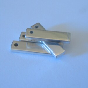 May include: Four silver metal rectangular bars with rounded edges and a small hole in the center of each bar.
