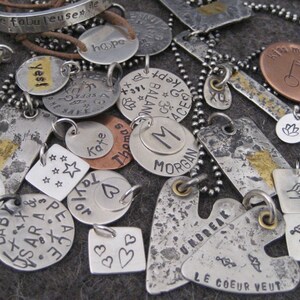 May include: A collection of silver and copper charm pendants with various words and designs, including "Protect Our Mother Earth", "fabulous", "hope", "yes", "balance", "Morgan", "Unbreak", "Le Coeur Veut", "vicki", and "143".