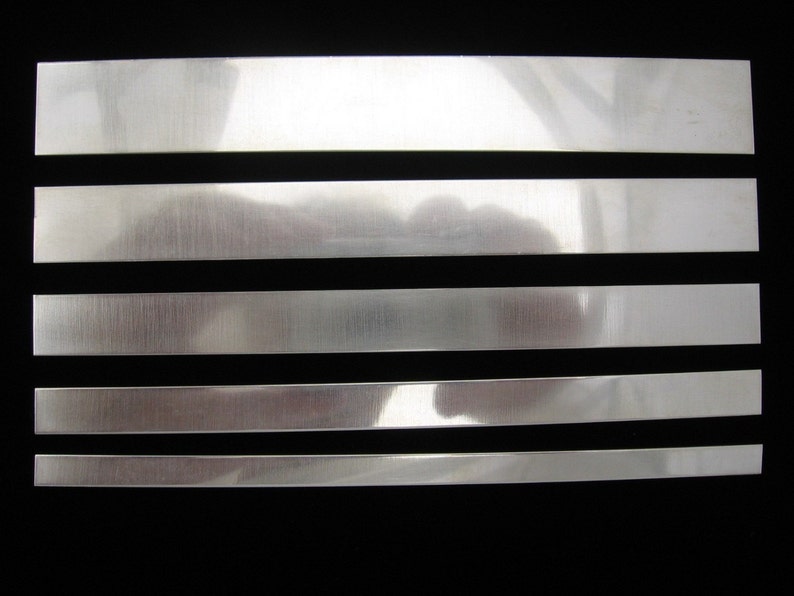 May include: Five silver metal strips of varying widths, arranged horizontally against a black background.