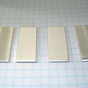 May include: Four rectangular silver metal bars arranged in a row on a white grid background.
