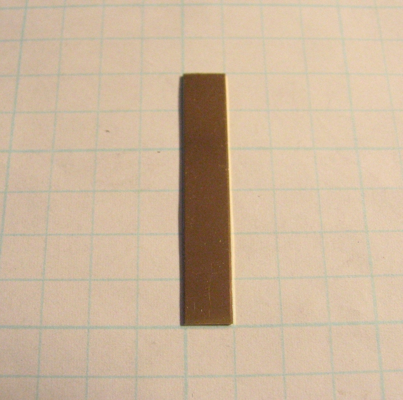 May include: A thin, rectangular piece of metal with a brown finish. It is approximately 2.5 cm wide and 7.5 cm long.