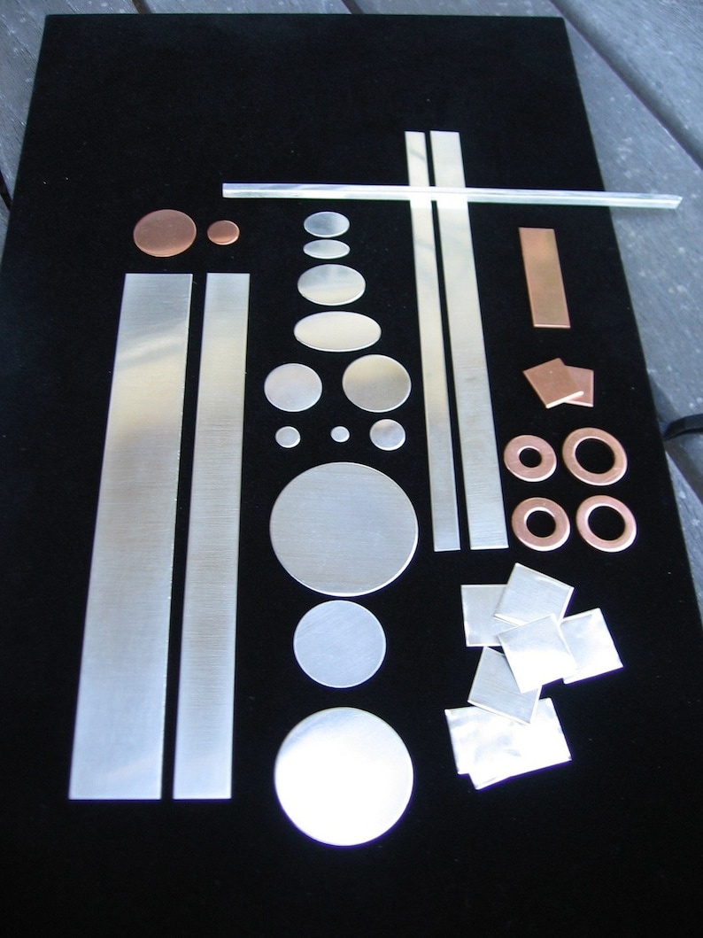 May include: Assortment of metal shapes and circles in various sizes, including silver and copper, on a black background.
