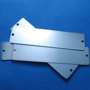 May include: Three silver metal rectangular name tags with rounded corners and holes punched in the top and bottom.