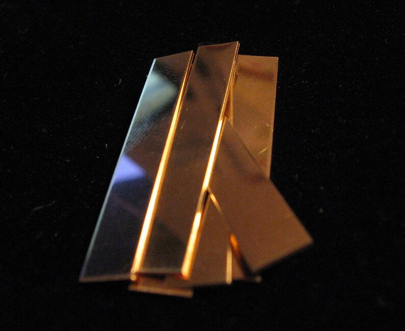May include: Four pieces of thin, flat, copper metal, stacked on top of each other. The copper is shiny and has a warm, golden colour.