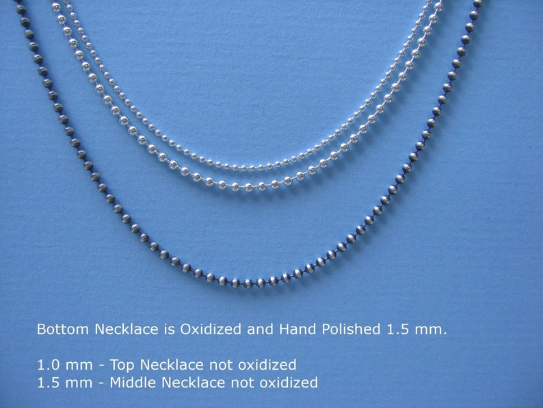 May include: Three silver ball chain necklaces on a blue background. The bottom necklace is oxidized and hand polished, measuring 1.5 mm. The middle necklace is not oxidized and measures 1.5 mm. The top necklace is not oxidized and measures 1.0 mm.