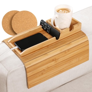 May include: A bamboo sofa arm tray with a built-in cup holder, remote control slot, and phone holder. Includes two round cork coasters. A white mug with a beverage and a black remote control are visible.