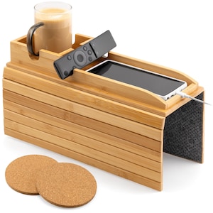 May include: A bamboo sofa arm tray with a built-in cup holder, remote control slot, and phone holder. A glass of coffee, a remote, and a smartphone are on the tray. Two cork coasters are in front of the tray.