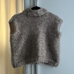 Peut inclure: Un pull sans manches en tricot brun et blanc avec un col montant.