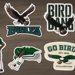 May include: A collection of Philadelphia Eagles-themed stickers. Designs include the team name, a flying eagle with a football, and a player in a green uniform. The stickers are in various shapes and sizes, with a distressed vintage aesthetic.