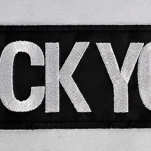 Op de afbeelding: Zwart rechthoekig embleem met de geborduurde tekst "FUCK YOU" in het wit. De patch heeft een zwarte rand en is waarschijnlijk bedoeld om op kleding of accessoires te worden genaaid of bevestigd.