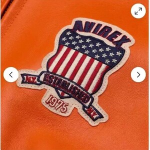 May include: Orange leather jacket with a patch featuring a shield with an American flag design and the text "Avirex Established 1975 NY."