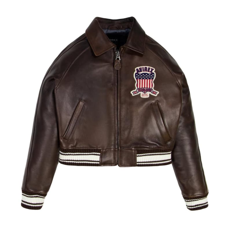 May include: A brown leather bomber jacket with a zip-up front, a collar, and a ribbed hem and cuffs with white stripes. The jacket features a patch on the chest with the text "AVIREX" and a patriotic design.