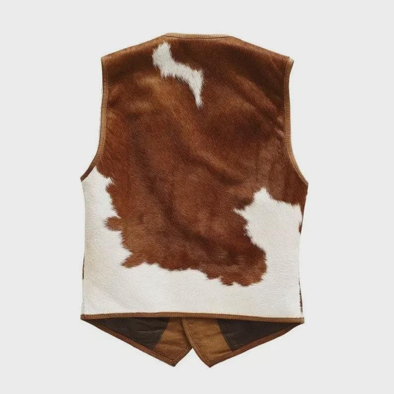May include: A brown and white cowhide vest with a V-neck and a two-button closure at the waist. The vest features a brown leather trim and a brown suede back panel. The vest is a western-style garment.