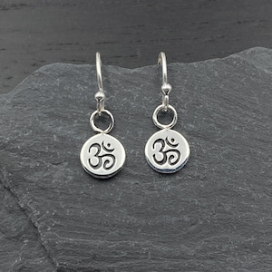 May include: A pair of silver earrings with a small, round charm featuring the Om symbol.