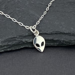 May include: A silver chain necklace with a small alien head pendant. The pendant is silver and has a detailed alien face with large eyes.