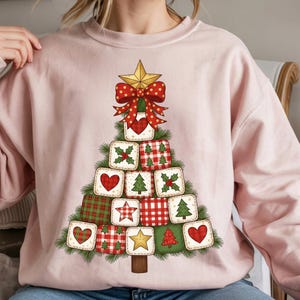 Peut inclure: Un sweat-shirt rose clair orné d'un motif de sapin de Noël. L'arbre est composé de blocs carrés avec des motifs variés, cœurs, étoiles et carreaux. Une étoile dorée et un nœud rouge ornent le sommet. Le design est festif et de saison.